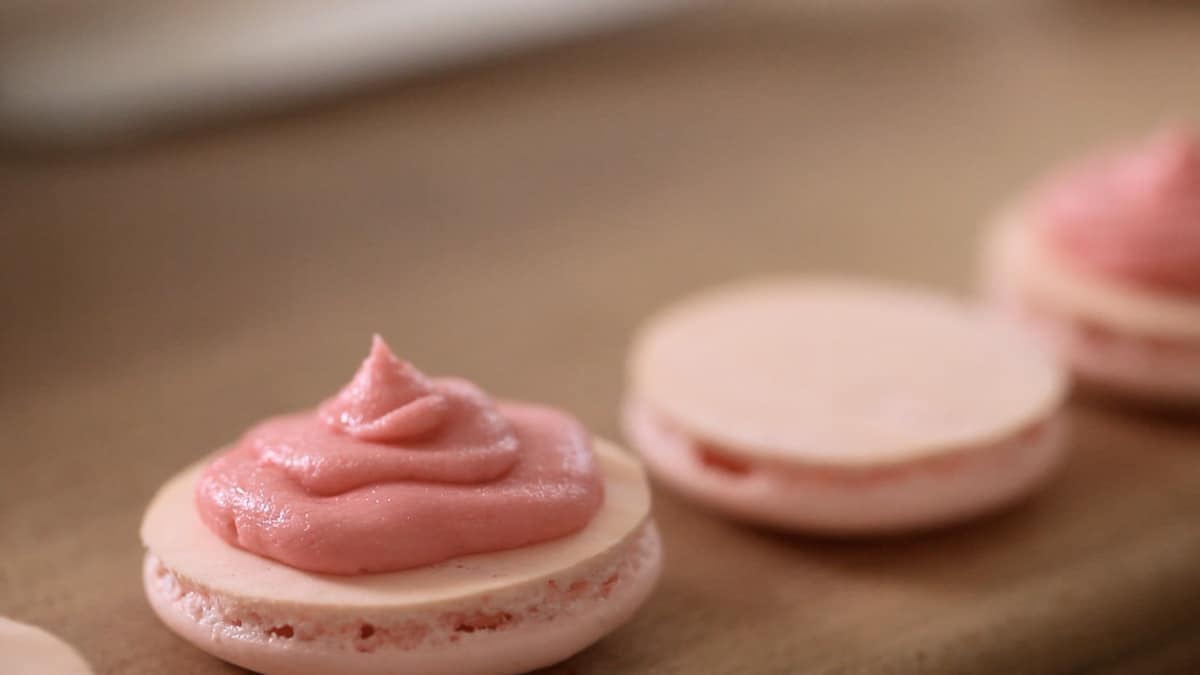 Making homemade French Macarons with raspberry coffee flavor: light pink,  unbaked macaron batter, so called macaronage, piped in circles on white parchment  paper before baking Stock Photo