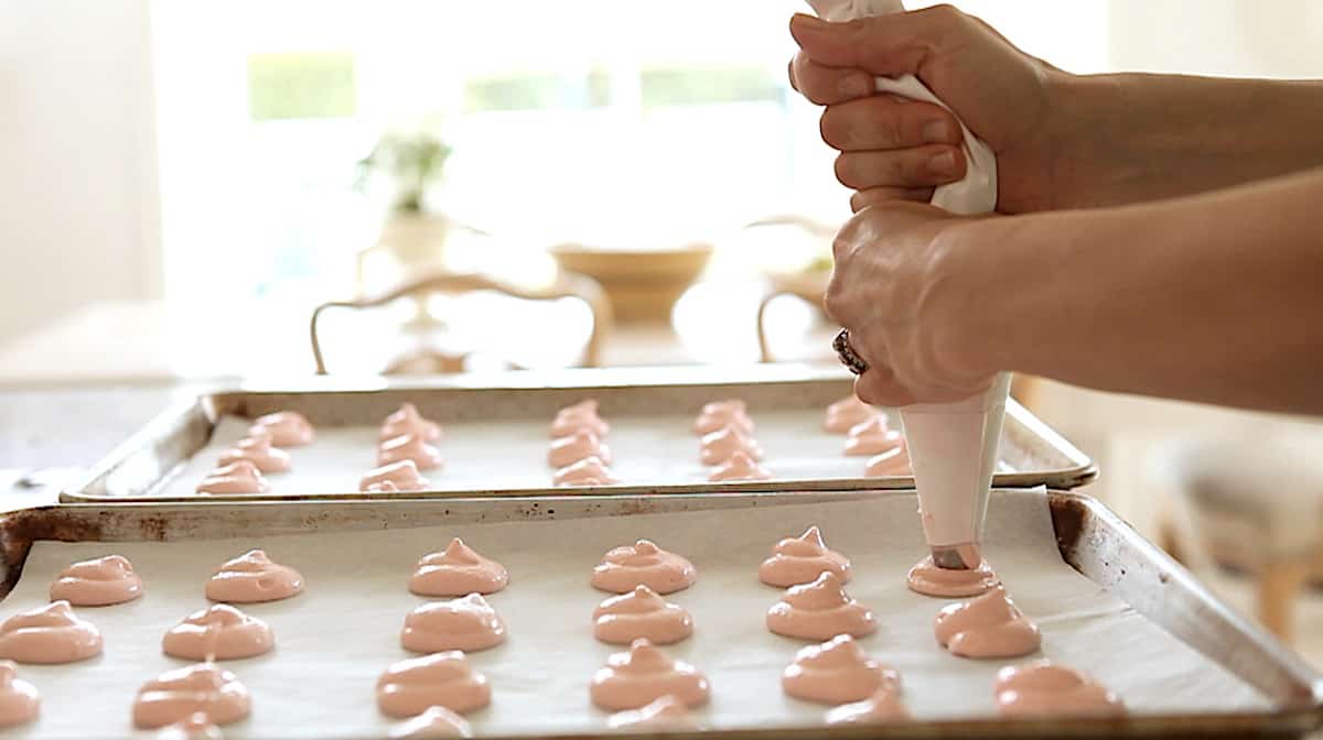 Piping macaron batter onto baking sheets with a pastry bag