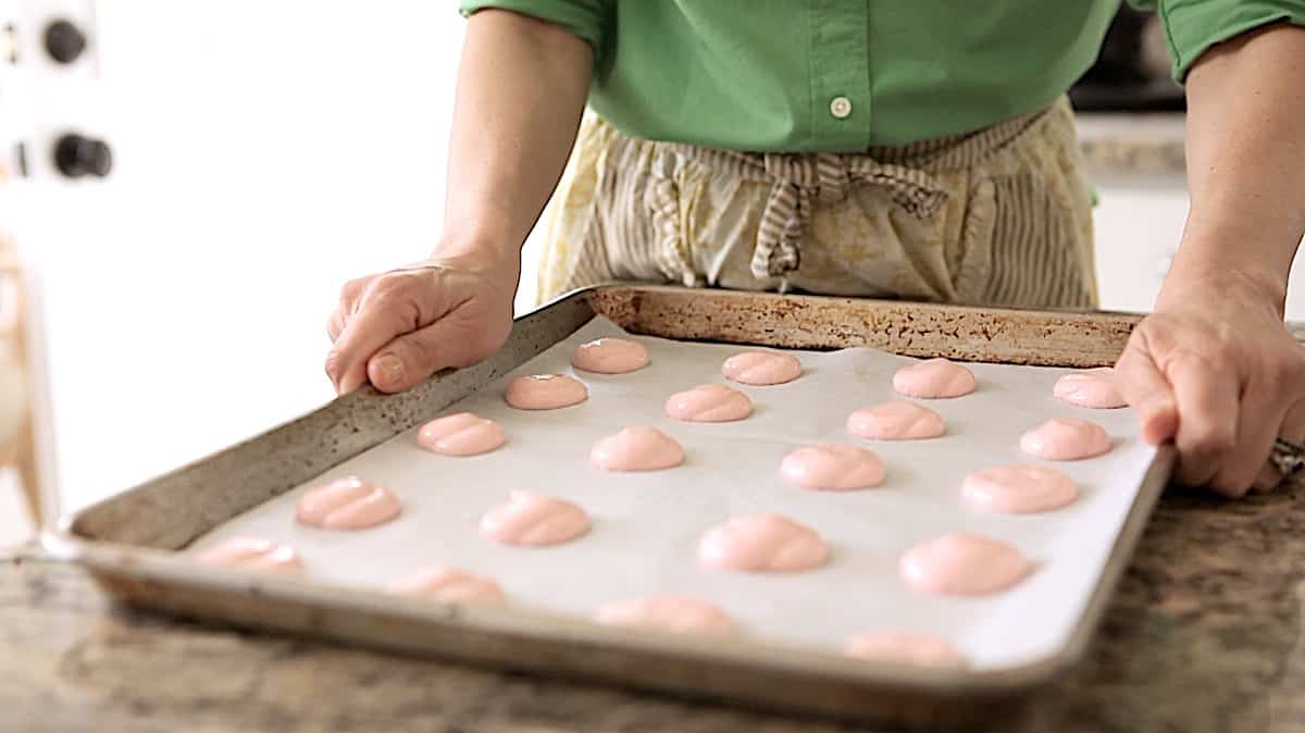 a person holding a tray of freshly piped French macaron cookies