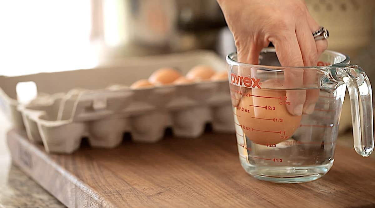 a person placing eggs into warm water in a pitcher