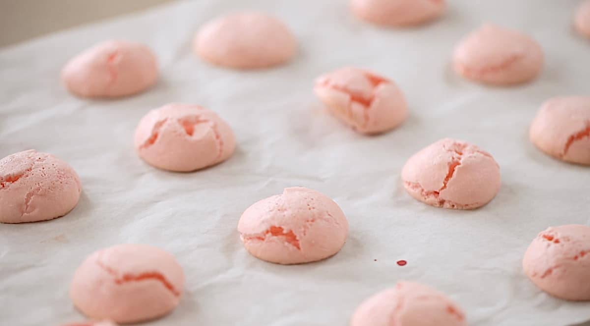 cracked macaron shells on a baking sheet with parchment paper