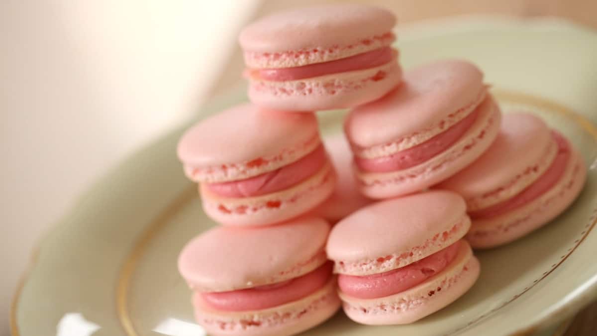 Pink French macarons filled with raspberry buttercream on a pale green cake stand