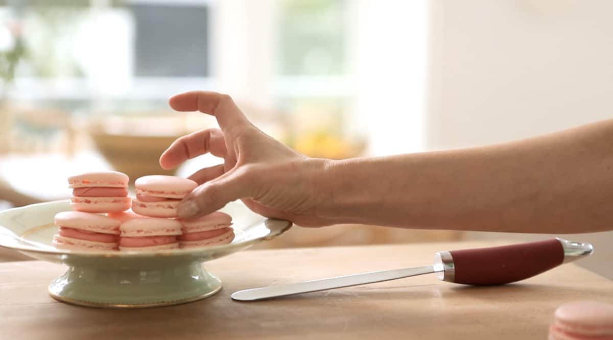 a person placing a finished French Macaron cookie on a cake stand