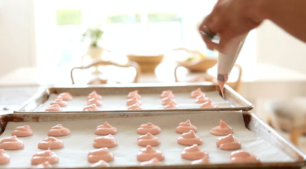 French Macarons being piped on a cookie sheet with a pastry bag