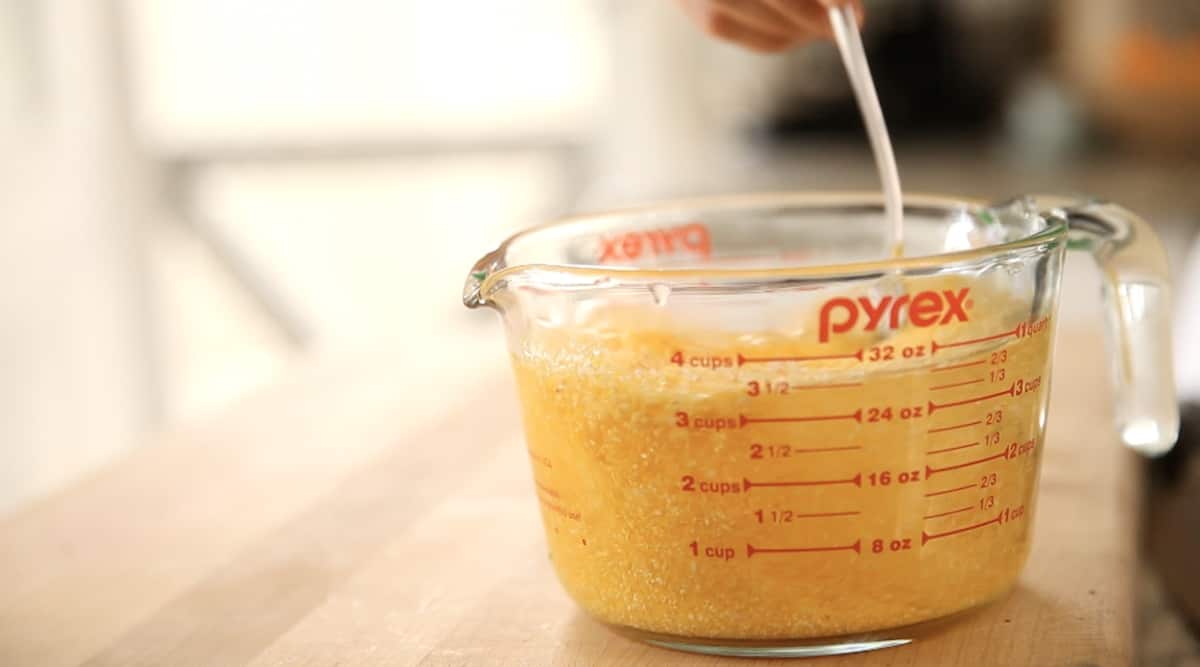 a person stirring water and polenta in a Pyrex pitcher