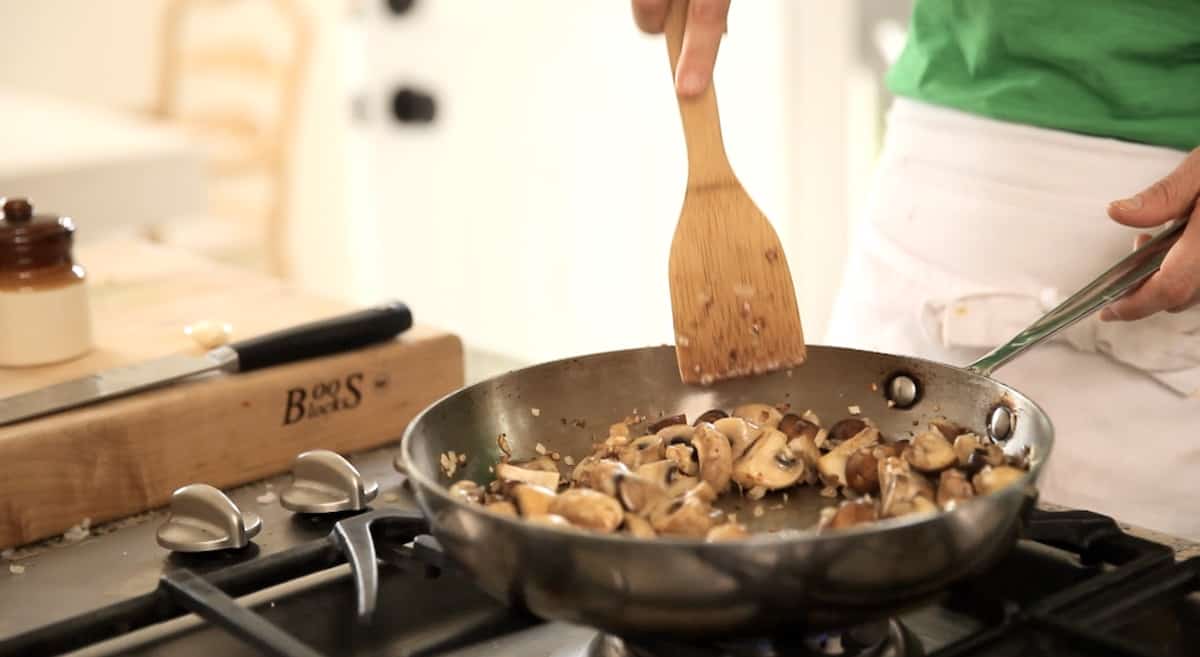 Cooking mushrooms in a pan with a wooden spoon