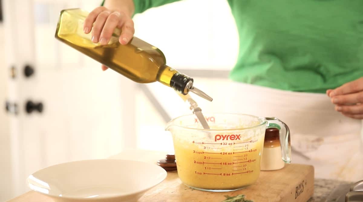 a person adding olive oil to cooked polenta in a Pyrex pitcher