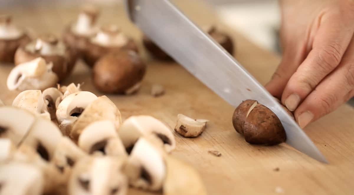 a person quartering mushrooms on a cutting board