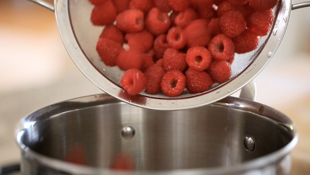 adding fresh raspberries to a sauce pot
