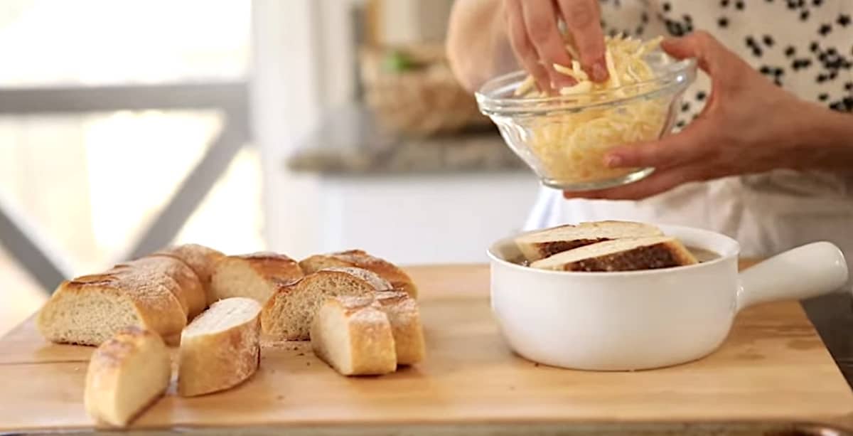Adding Grated Gruyere Cheese to sliced bread in a soup bowl