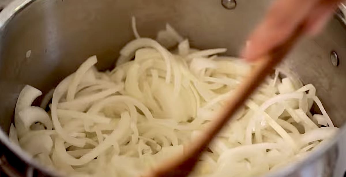 Sliced white onions in a large stock pot with a wooden sppon