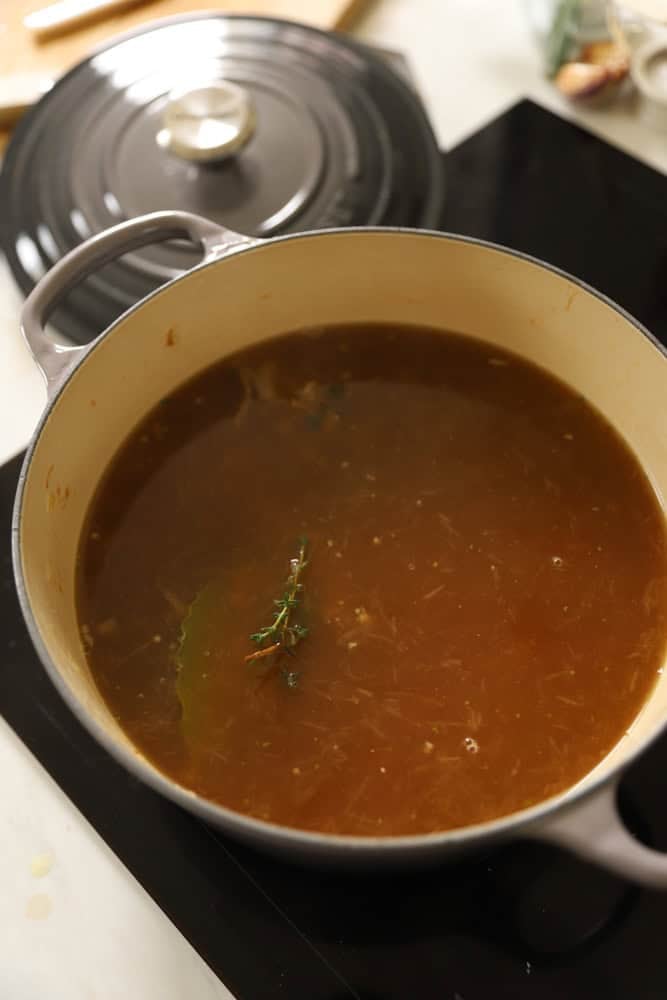 Beef broth simmering in a Dutch oven with herbs and onions.