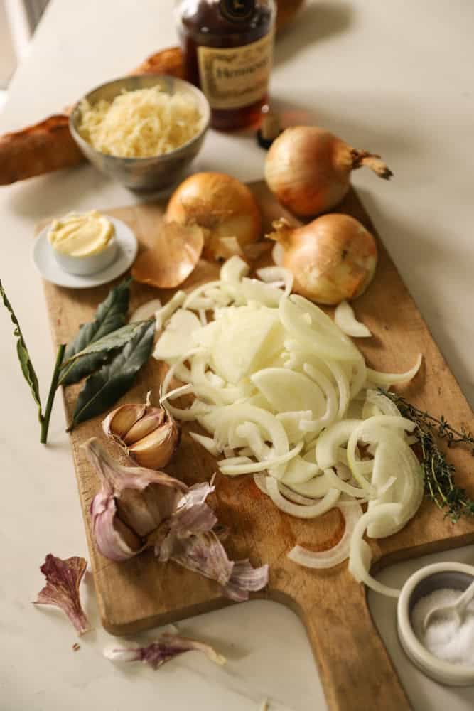 Sliced onions, herbs, cheese and bread laid out on a cutting board.