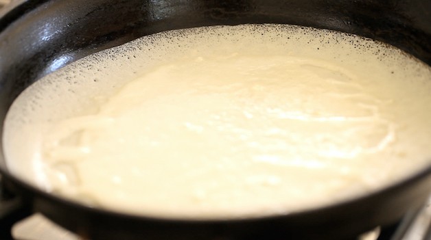 crepe batter cooking in black pan