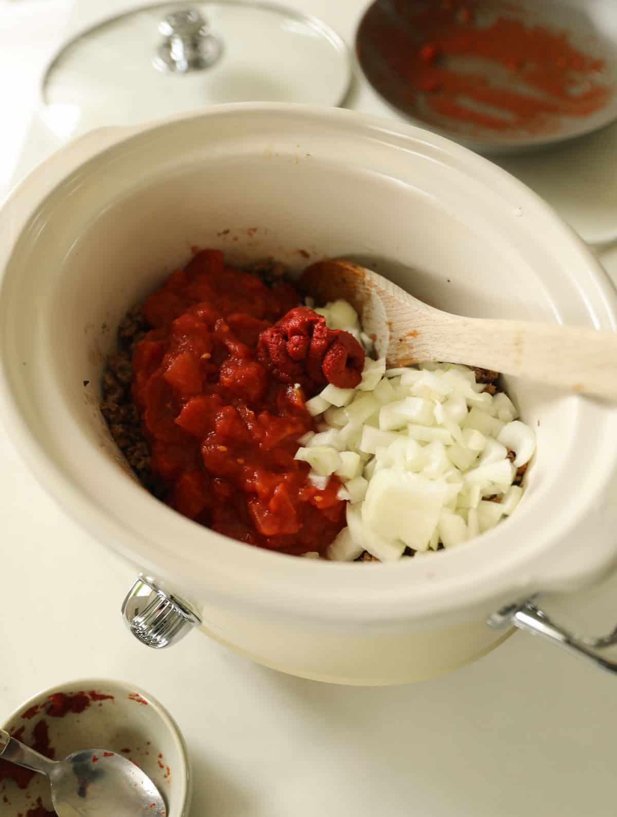 a slow cooker filled with onion, tomatoes and cooked ground beef.