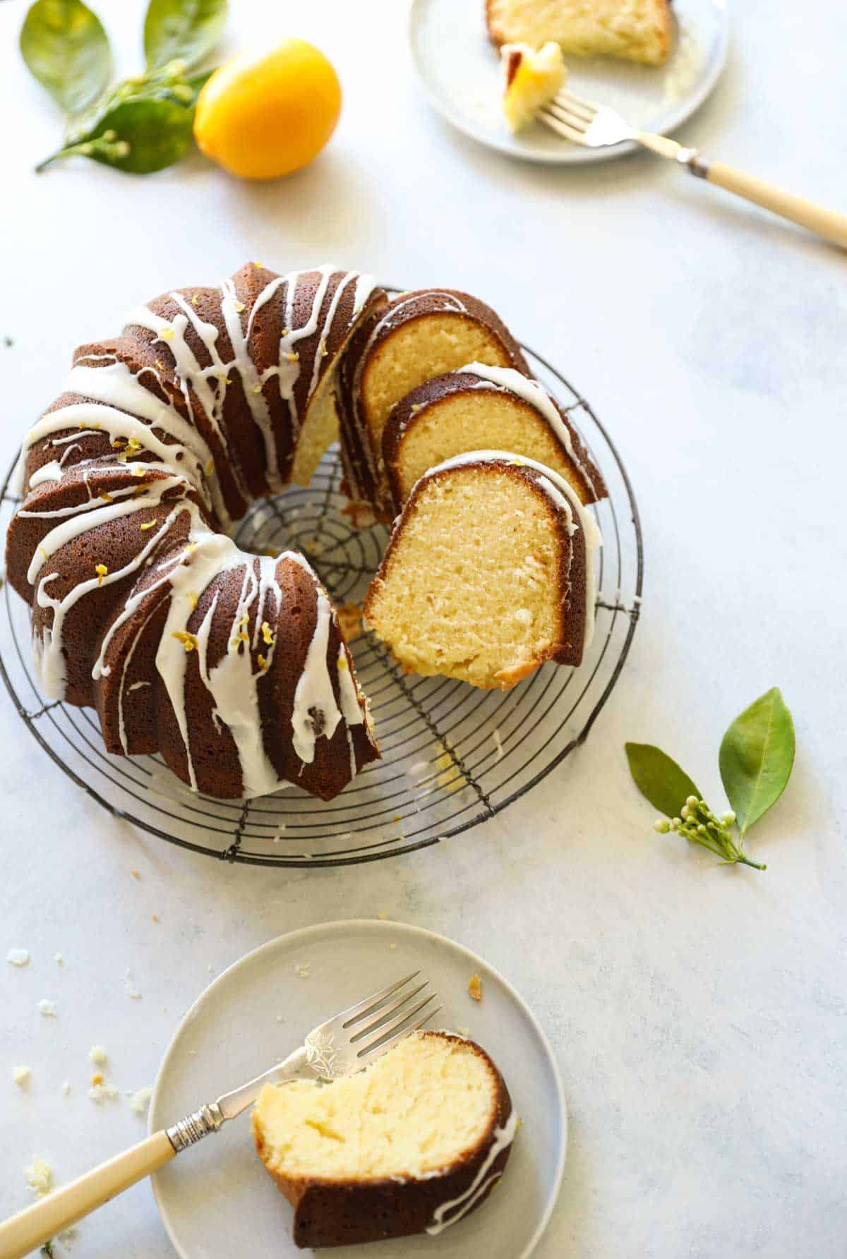 a lemon bundt cake on a cake stand sliced with plates of cake with forks