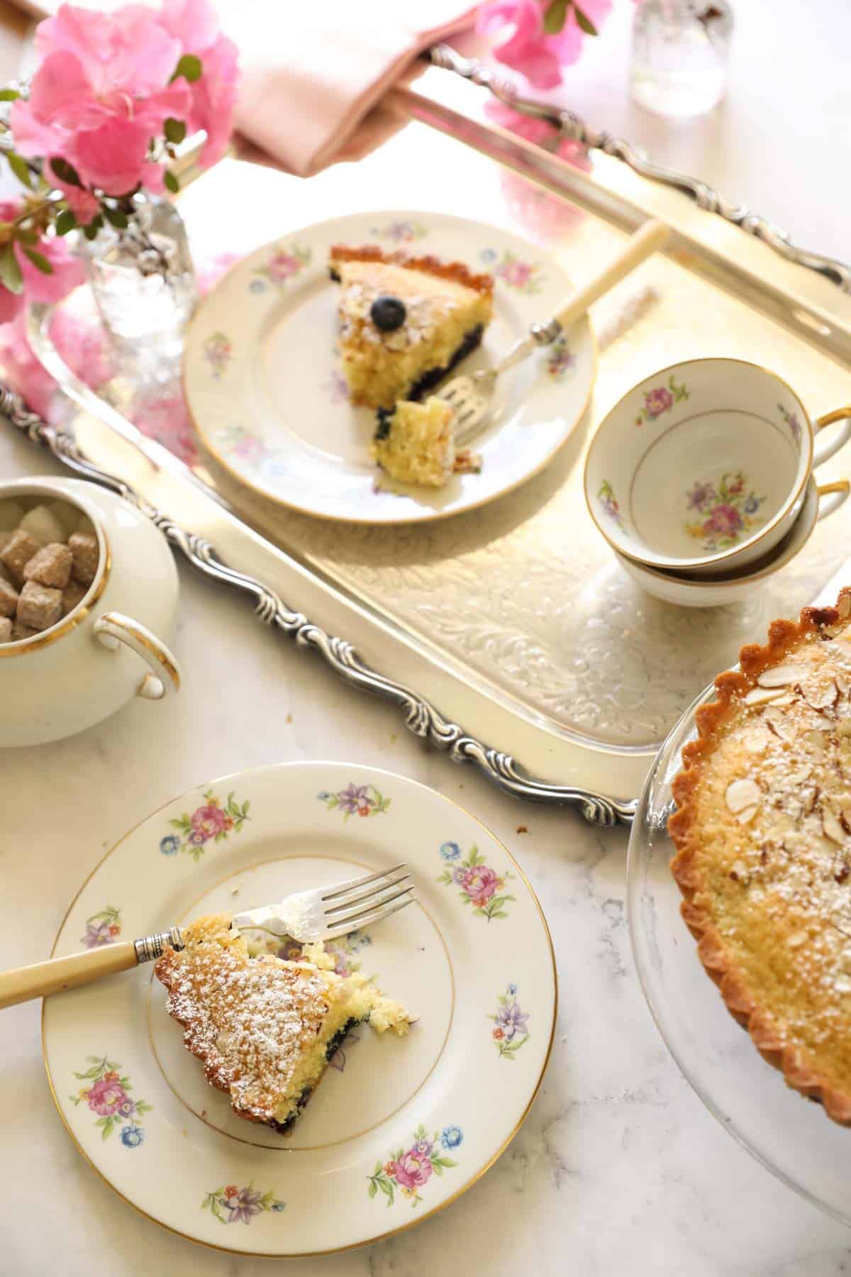 a large tea party scene with slices of cake and tea cups on a silver tray