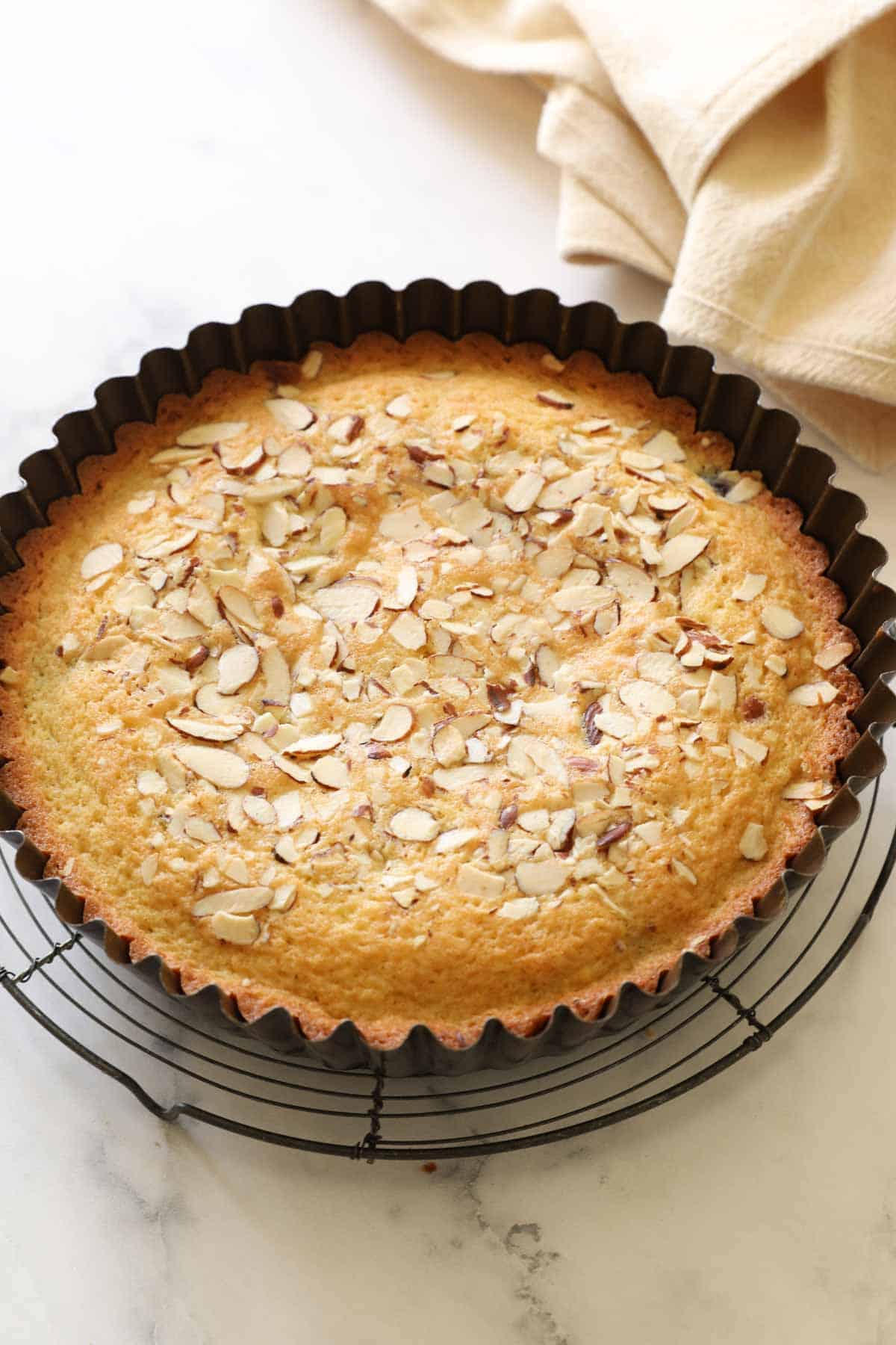 a cake with almonds on top cooling in a tart tin