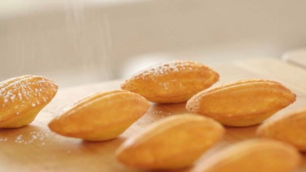 Madeleines on board being dusted with powdered sugar