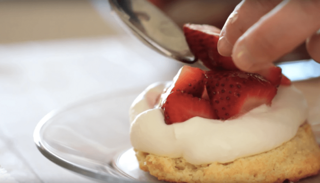 Placing strawberries on top of a shortcake biscuit with whipped cream