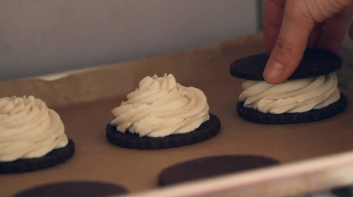 a person placing a chocolate cookie on top of another to form a sandwich in the freezer