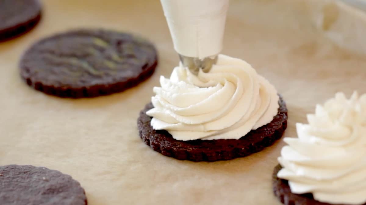 a piping bag piping ice cream filling onto a chocolate cookie