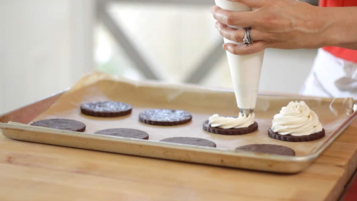 a person piping ice cream filling on to cookie rounds