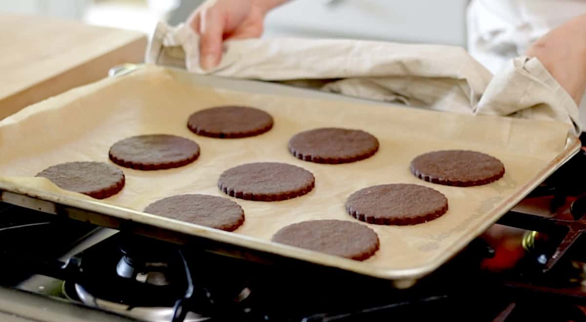 a person brining a tray of freshly baked chocolate cookies to the cook top