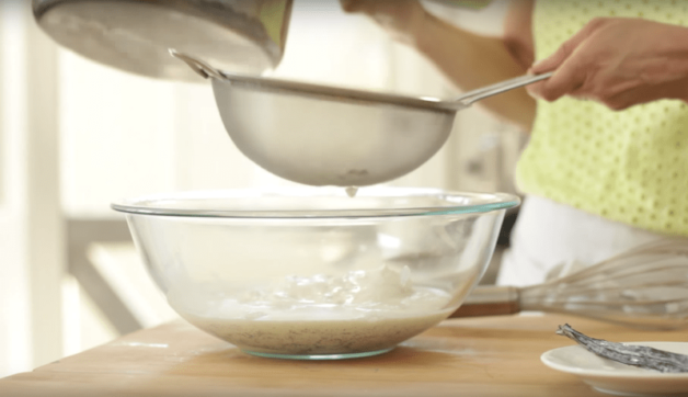 milk mixture being strained into yogurt in a clear bowl
