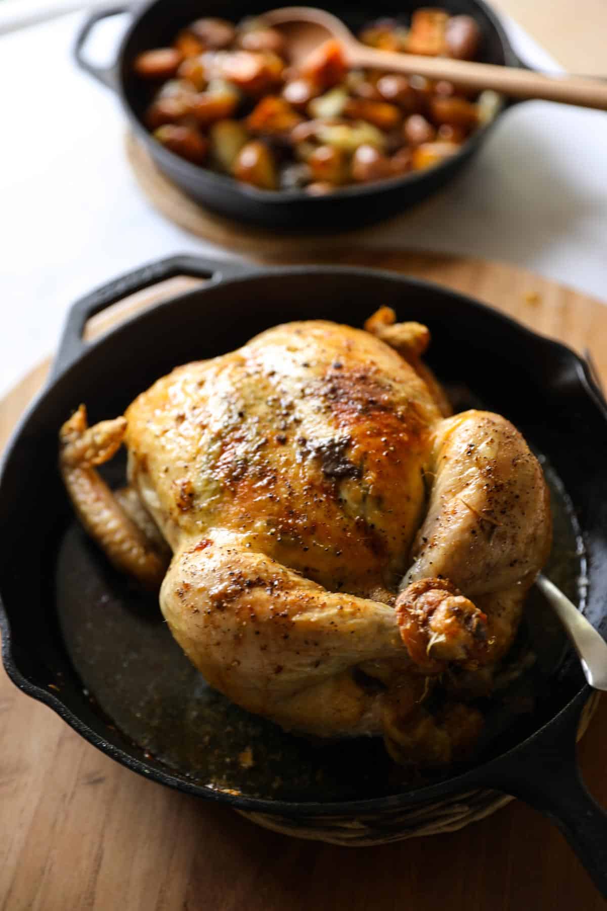 a roasted chicken in a cast iron skillet with a skillet of roasted root vegetables