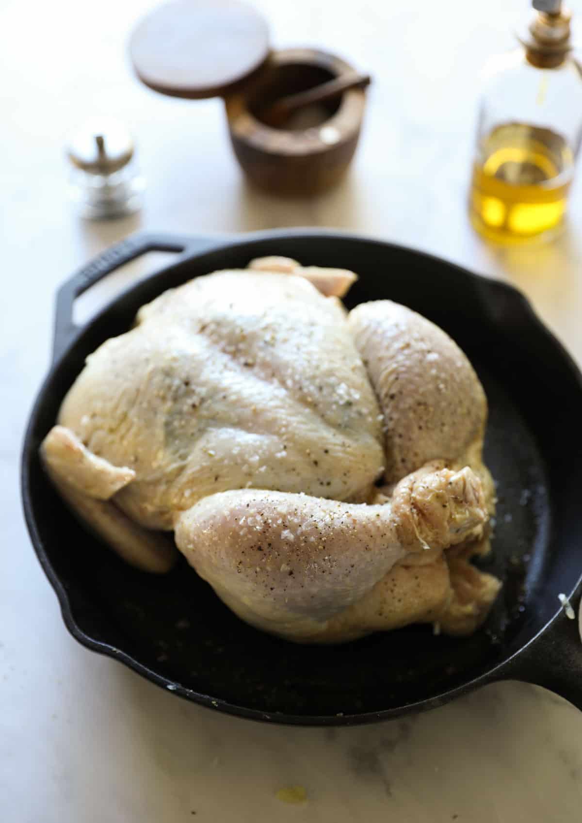 a raw trussed chicken in a cast iron skillet