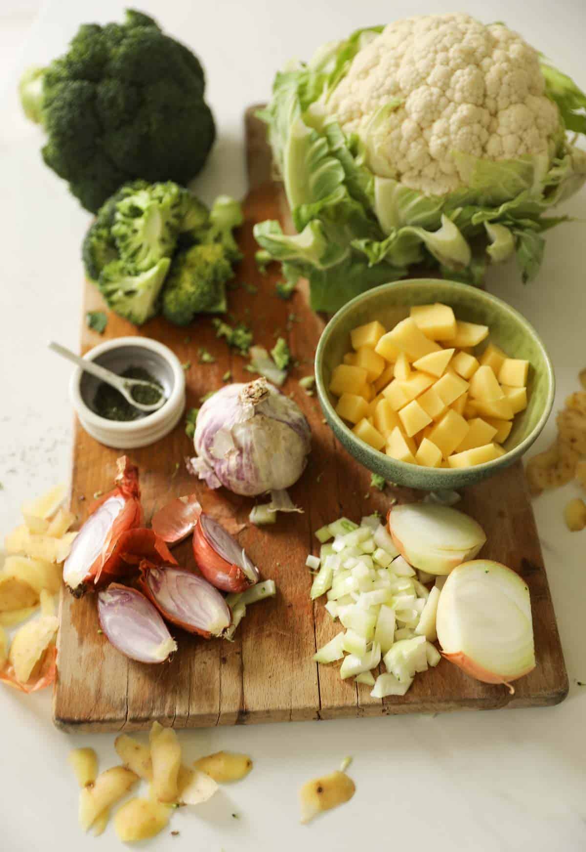 Broccoli, Cauliflower, Potato and onions laid out on a cutting board for making soup.