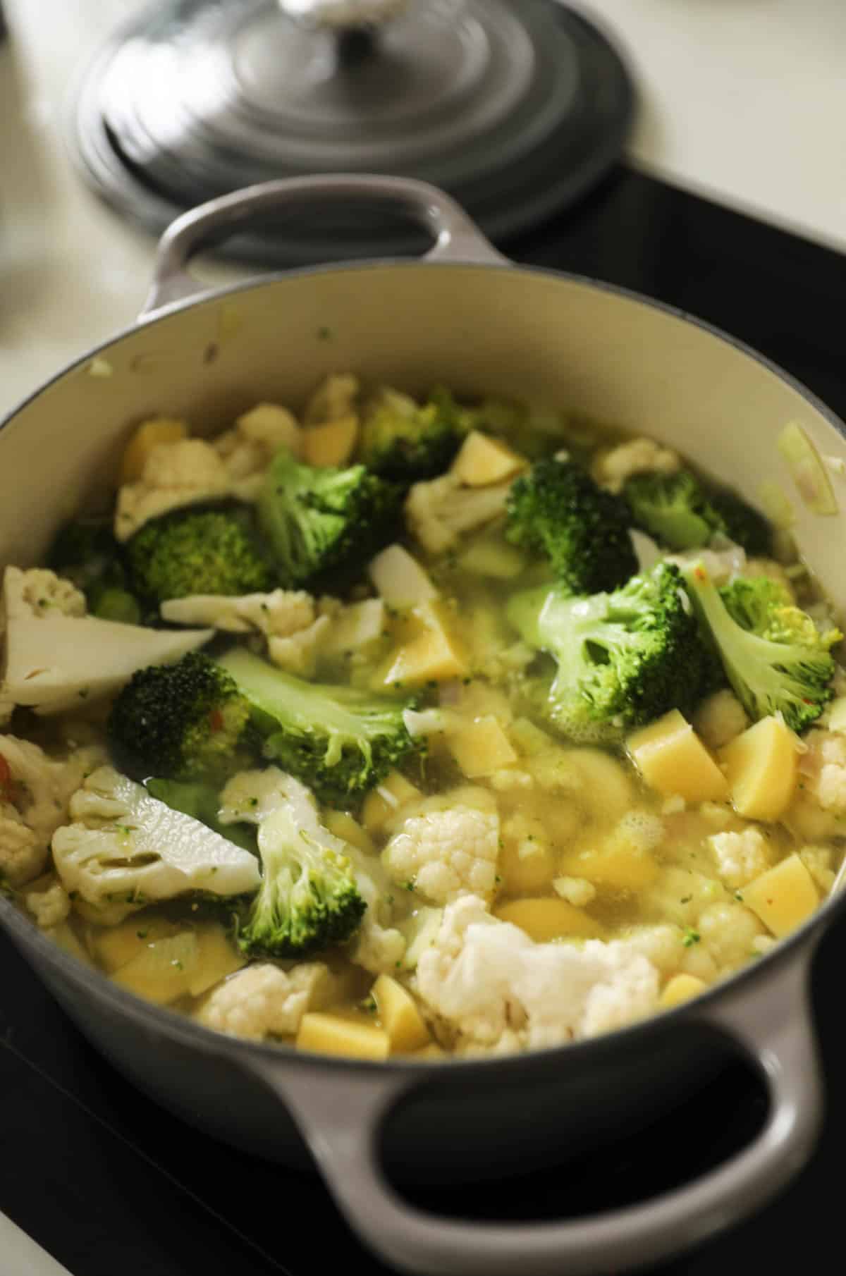 A large soup pot filled with broccoli, cauliflower, potatoes, onions and broth.