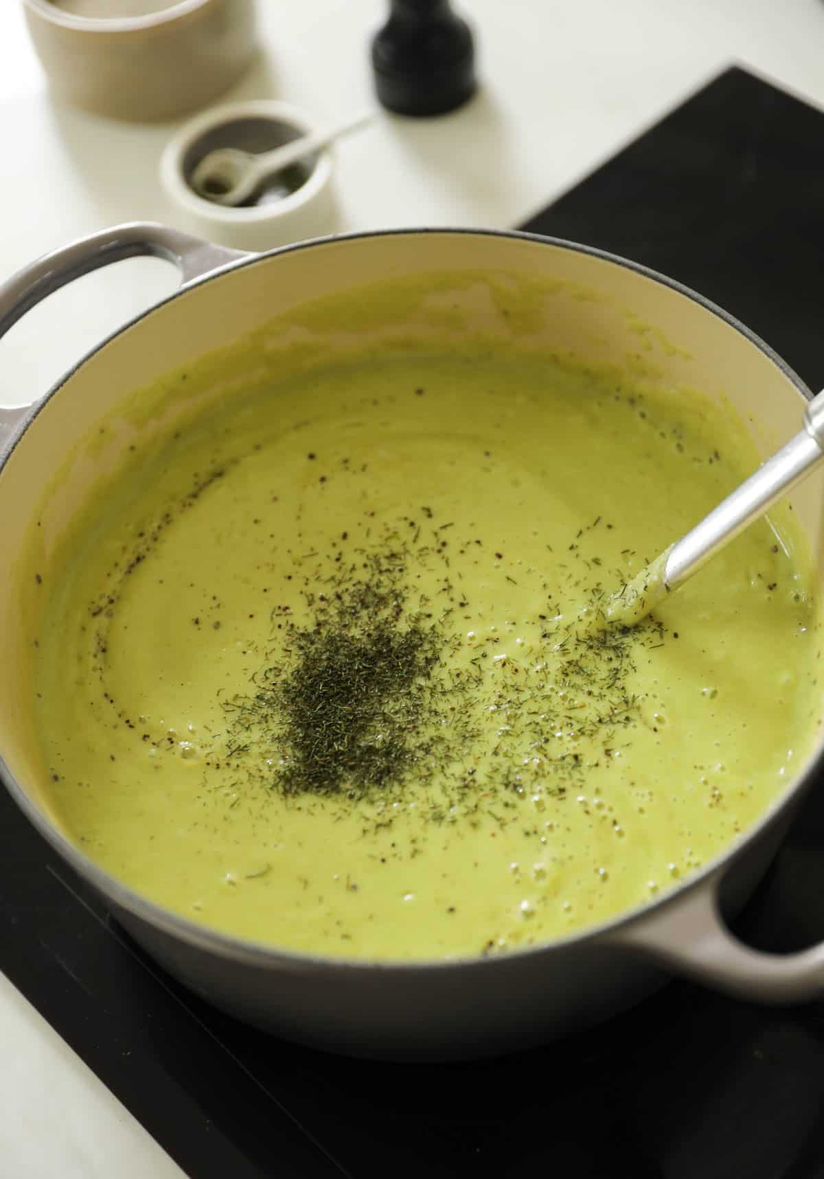 A large pot of creamy broccoli soup with drilled dill added and a ladle.