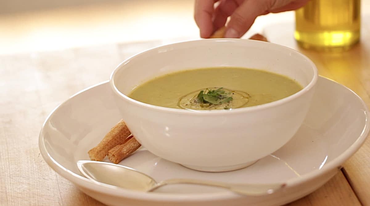 a person adding breadsticks to a Vegan cream of broccoli soup