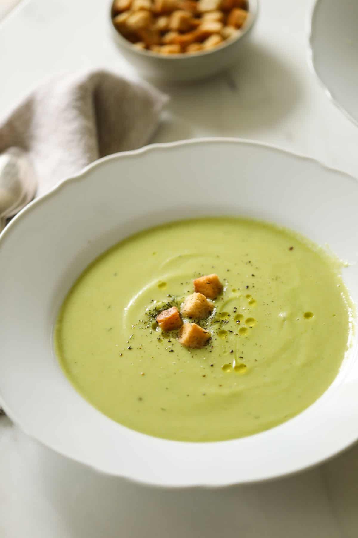 Cream of broccoli soup in a white bowl with croutons.