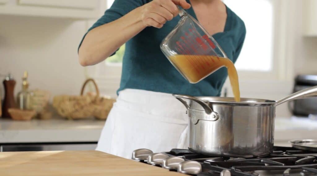 adding vegetable broth to a sauce pot from a pitcher