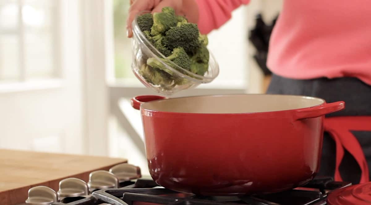 adding broccoli to a large red pot