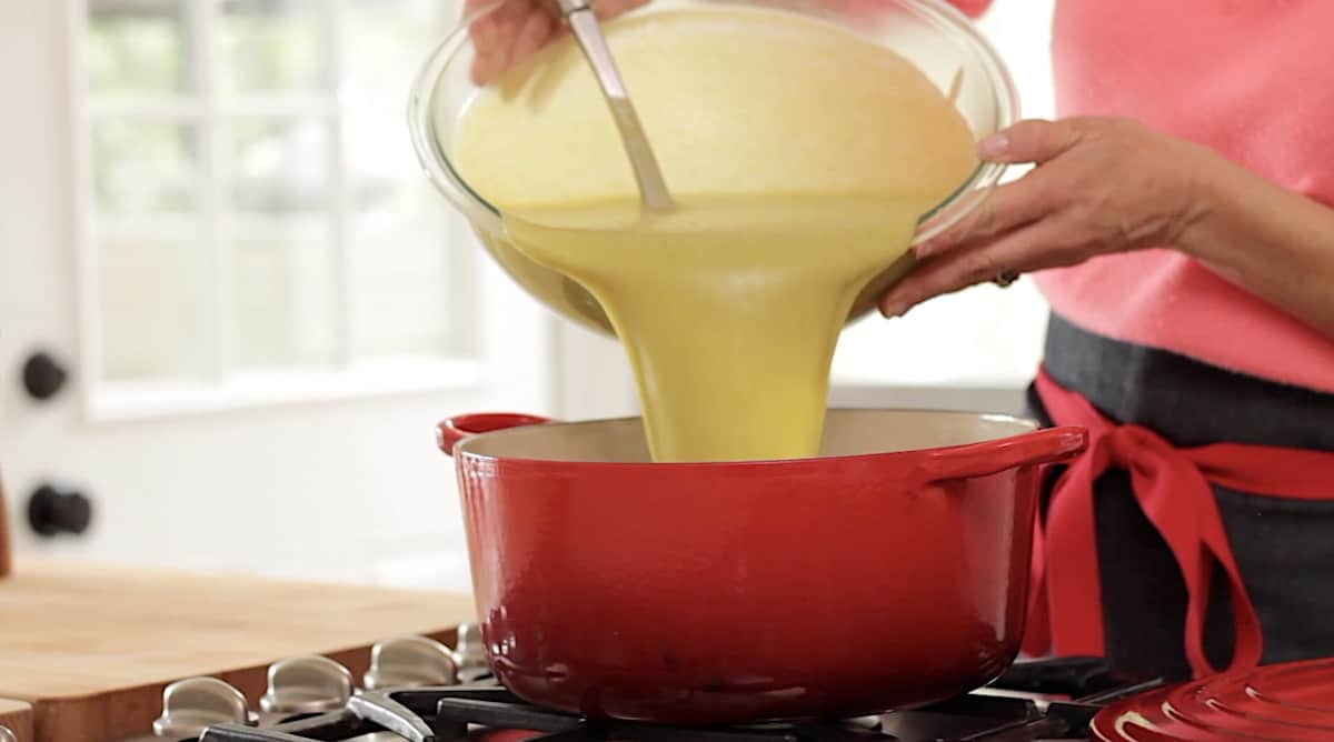 transferring cream of broccoli soup into a large red soup pot