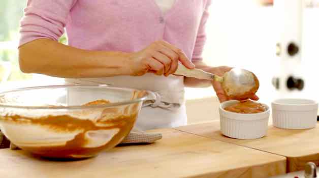 Spooning chocolate souffle batter into white ramekins until they are full