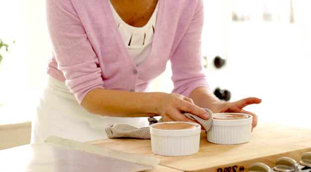 Cleaning the sides of two white souffle ramekins with a clean dish towel