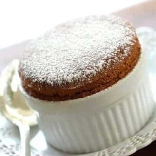 Freshly baked Chocolate Souffle in ramekin sitting on a white plate with silver spoon 