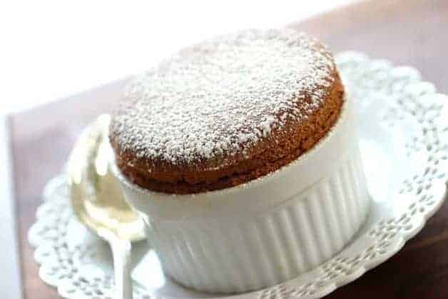 Freshly baked Chocolate Souffle in ramekin sitting on a white plate with silver spoon 