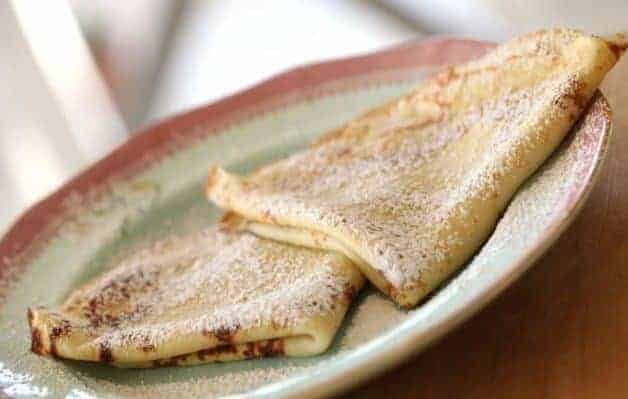 2 folded crepes on a blue plate with powdered sugar