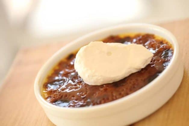 A Crème brûlée served in a white ramekin topped with whipped cream