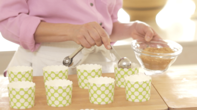 A person adding graham cracker crumbs to green cupcake liners 