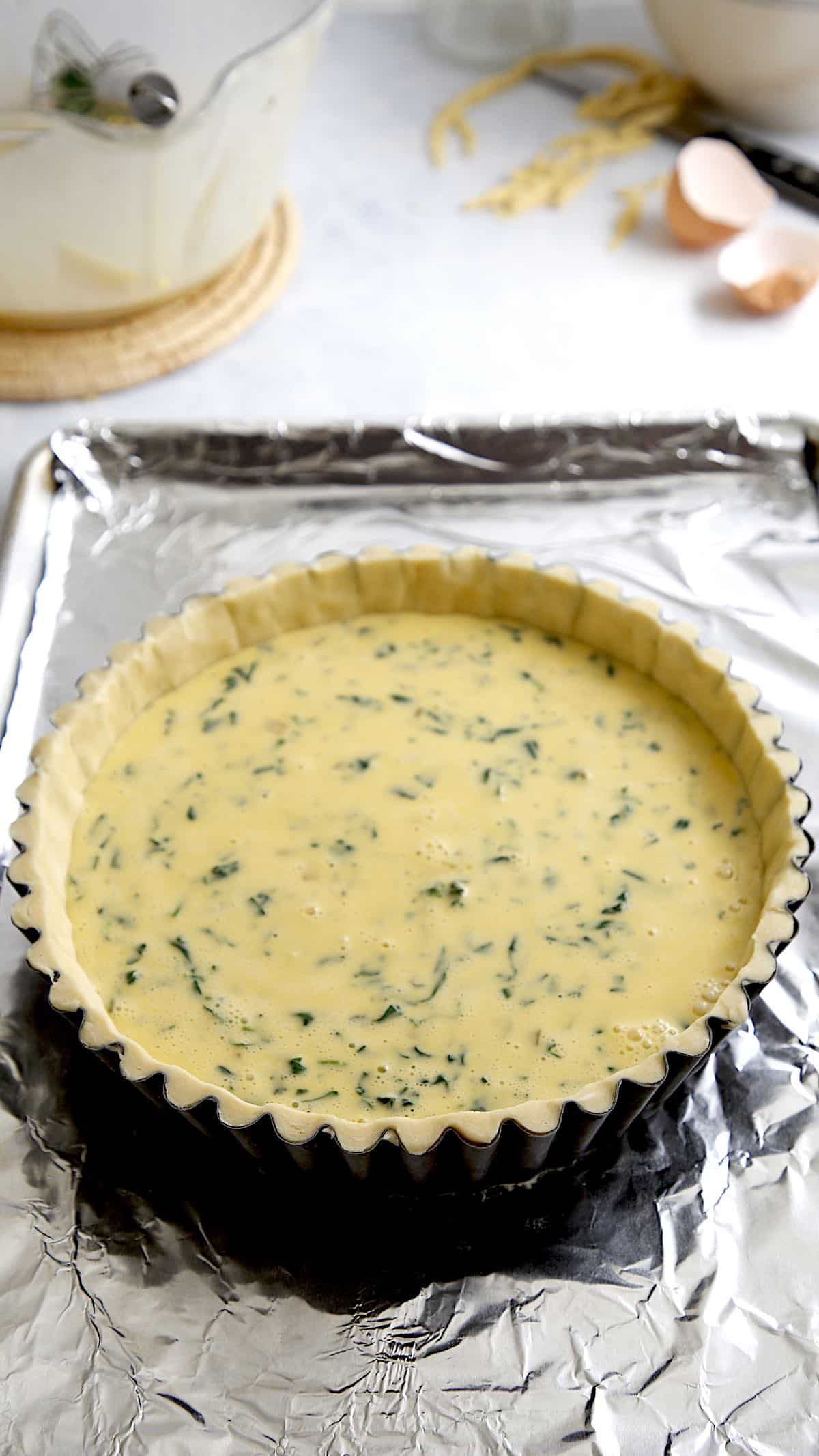 Quiche filled in a tin on a baking sheet before baking