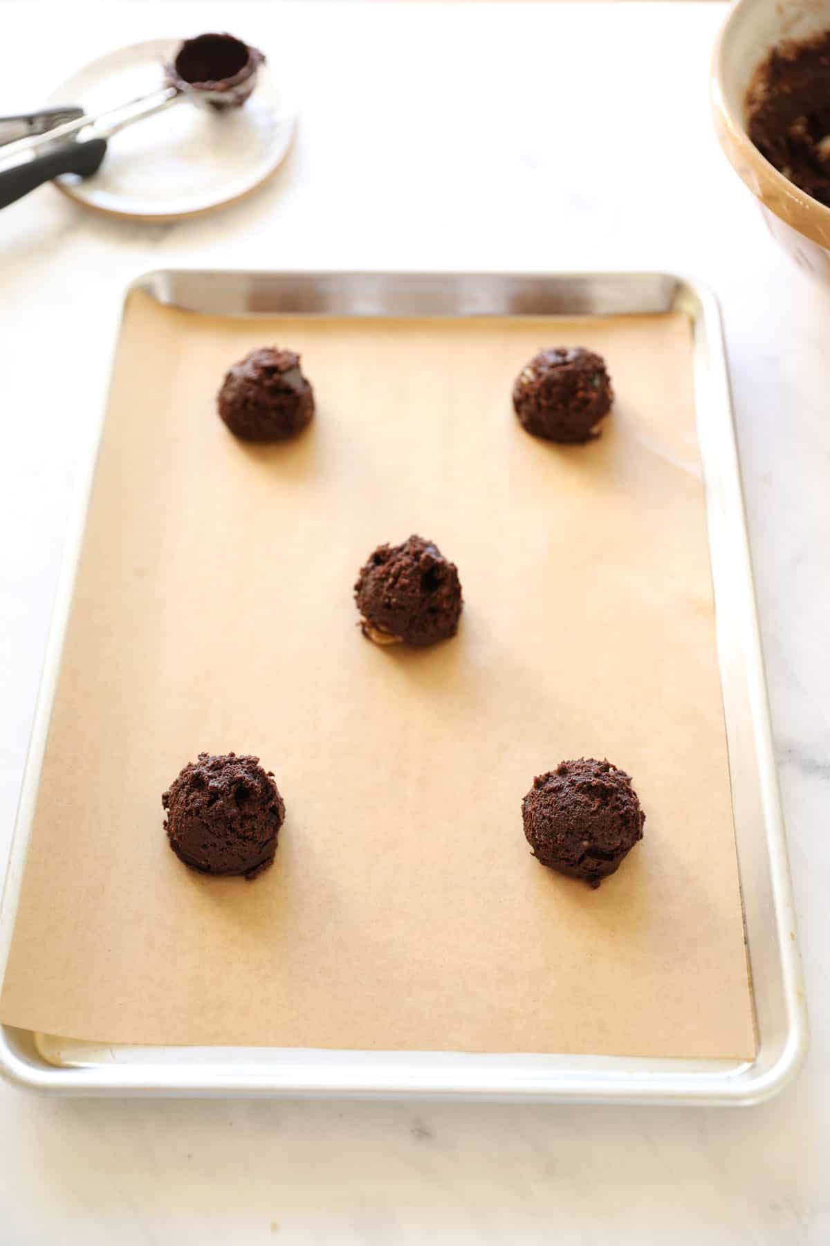 chocolate cookie scoop dough placed on a sheet tray with parchment paper lining