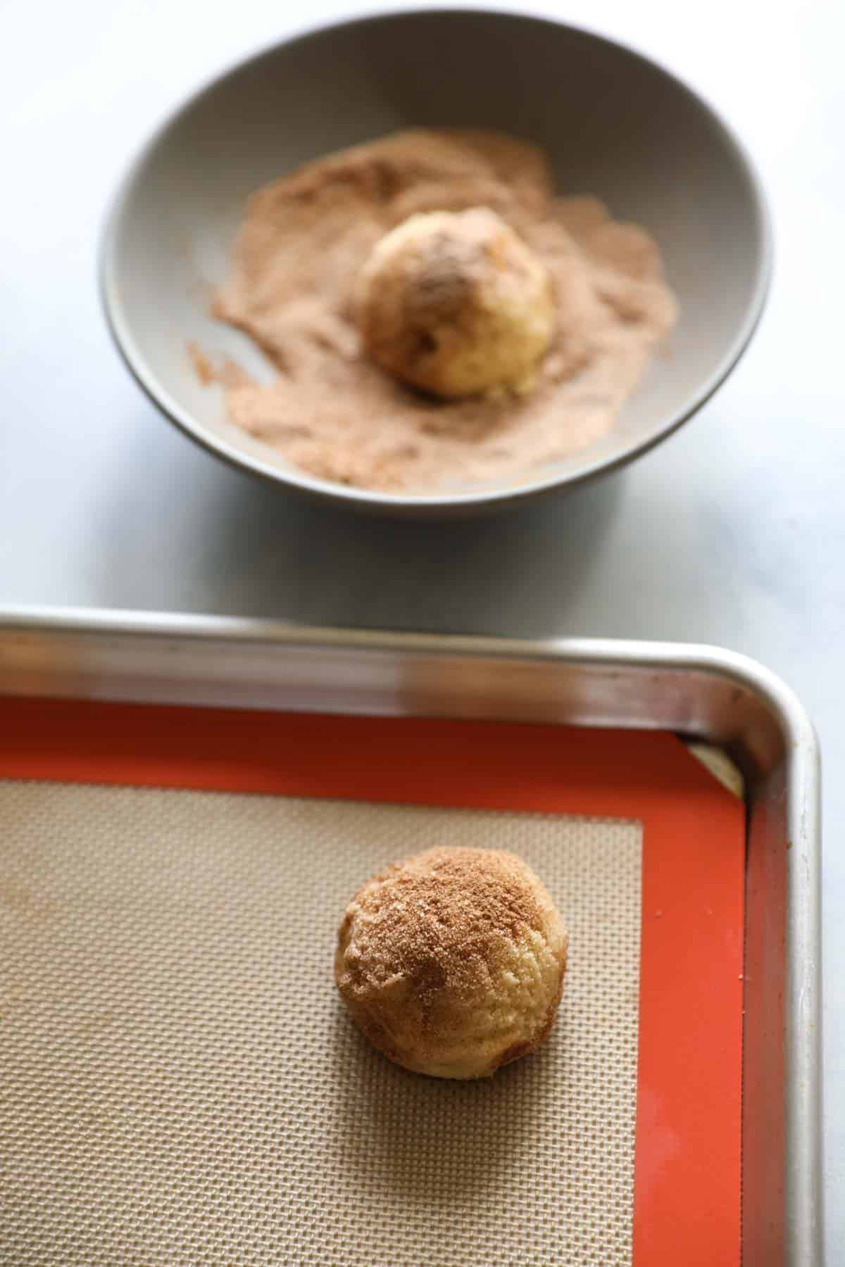 cookie dough ball being rolled in cinnamon sugar