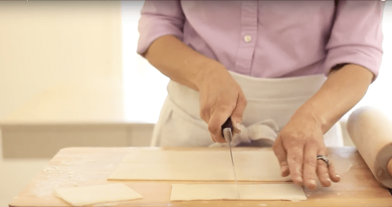 a person slicing puff pastry into squares on a cutting board
